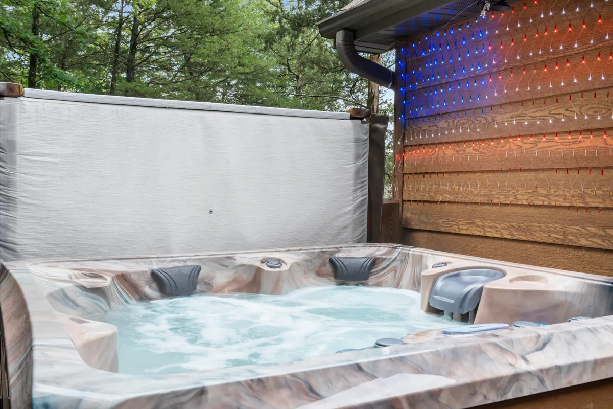 A serene outdoor jacuzzi set against a rustic wooden wall and soft, decorative lighting. The ambiance is tranquil and private, ideal for quiet reflection or reconnecting with loved ones under the stars.