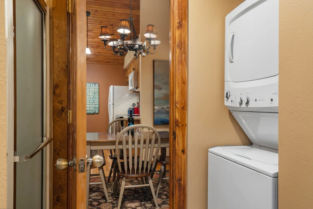 A bright and inviting space featuring a dining table, elegant chandelier, and a discreet washer/dryer tucked into the corner. The room exudes warmth and highlights thoughtful amenities that make longer stays convenient and comfortable.