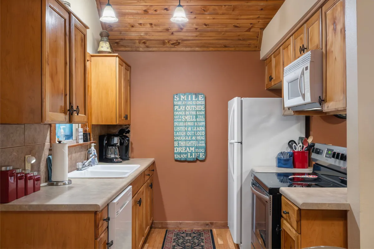 A cheerful kitchen interior with wooden cabinetry, modern appliances, and motivational wall art. The space is well-lit and organized, clearly ready for cooking family favorites or hosting gatherings.