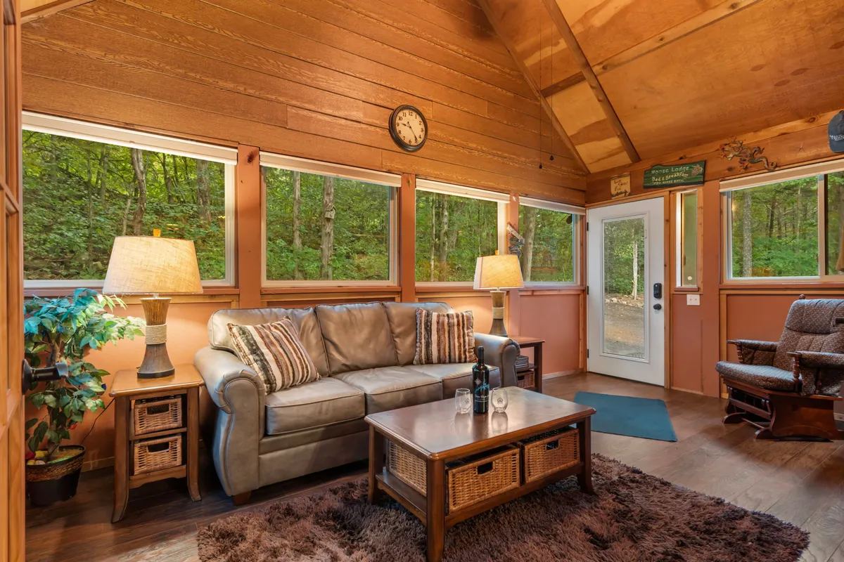 A welcoming lounge area featuring a sofa, coffee table, table lamps, and large windows with scenic views. The design blends comfort and nature, making the room perfect for relaxing, reading, or sharing quiet moments with others.