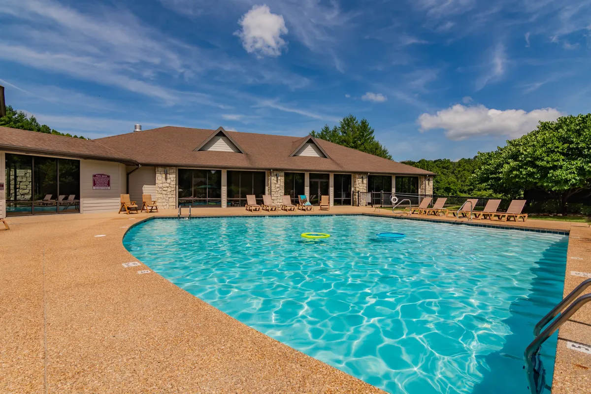 A vibrant outdoor pool surrounded by lounge chairs and lush greenery, with the resort's building façade visible in the background. The inviting water and relaxed seating area suggest a family-friendly atmosphere perfect for warm weather activities.