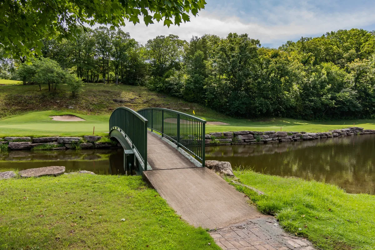 A serene scene featuring a picturesque bridge over water, with the golf course and trees in the background. The tranquil water and well-kept greens evoke a sense of relaxation and outdoor enjoyment.