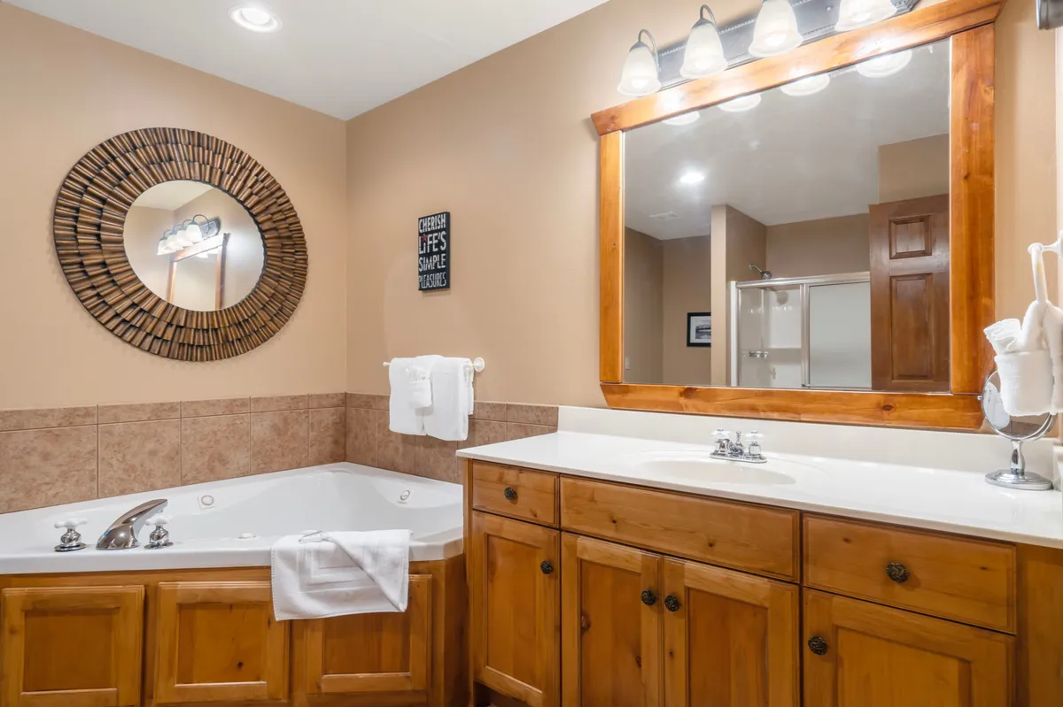 A calming bathroom scene with a large jacuzzi tub, a spacious wooden vanity, a decorative mirror, and soft, natural lighting. The space invites guests to indulge in spa-like relaxation and self-care routines.