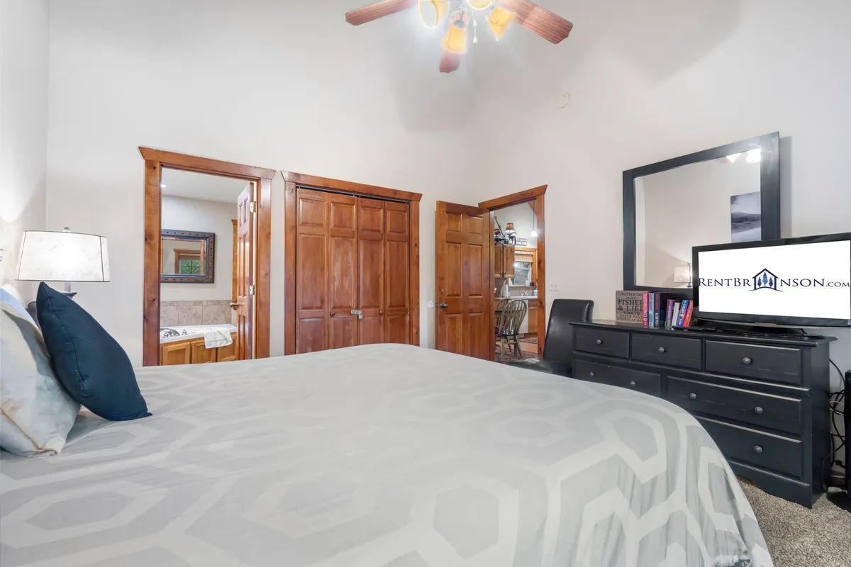 A relaxing bedroom setting with a bed featuring a patterned comforter, a nightstand with a lamp, a framed mirror above dressers, and a TV in the room. The space feels quiet and serene—ideal for unwinding at the end of the day or enjoying peaceful moments in the morning.