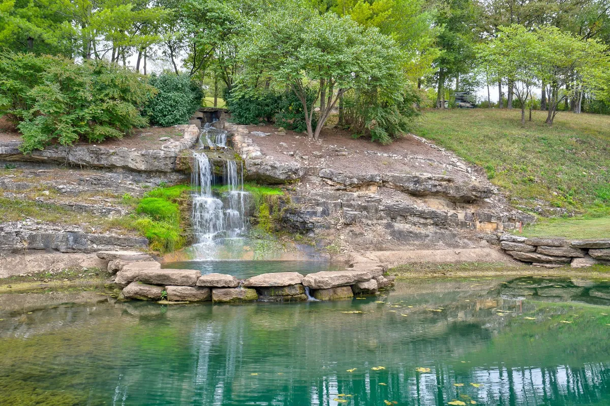 A tranquil exterior view of a waterfall and pond with rock formations and trees, inviting opportunities for fishing, nature walks, or simply enjoying the peaceful scenery.